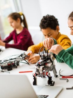 Group of happy kids programming electric toys and robots at robotics classroom