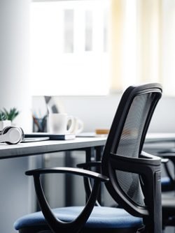 Modern gadgets in interior of coworking office during COVID-19 epidemic. Chairs and desk for support workers, laptops and headphones, cups and stationery in daylight on window background, free space
